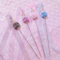 Set of decorative sticks with colorful pom-pom ends on a textured pink background