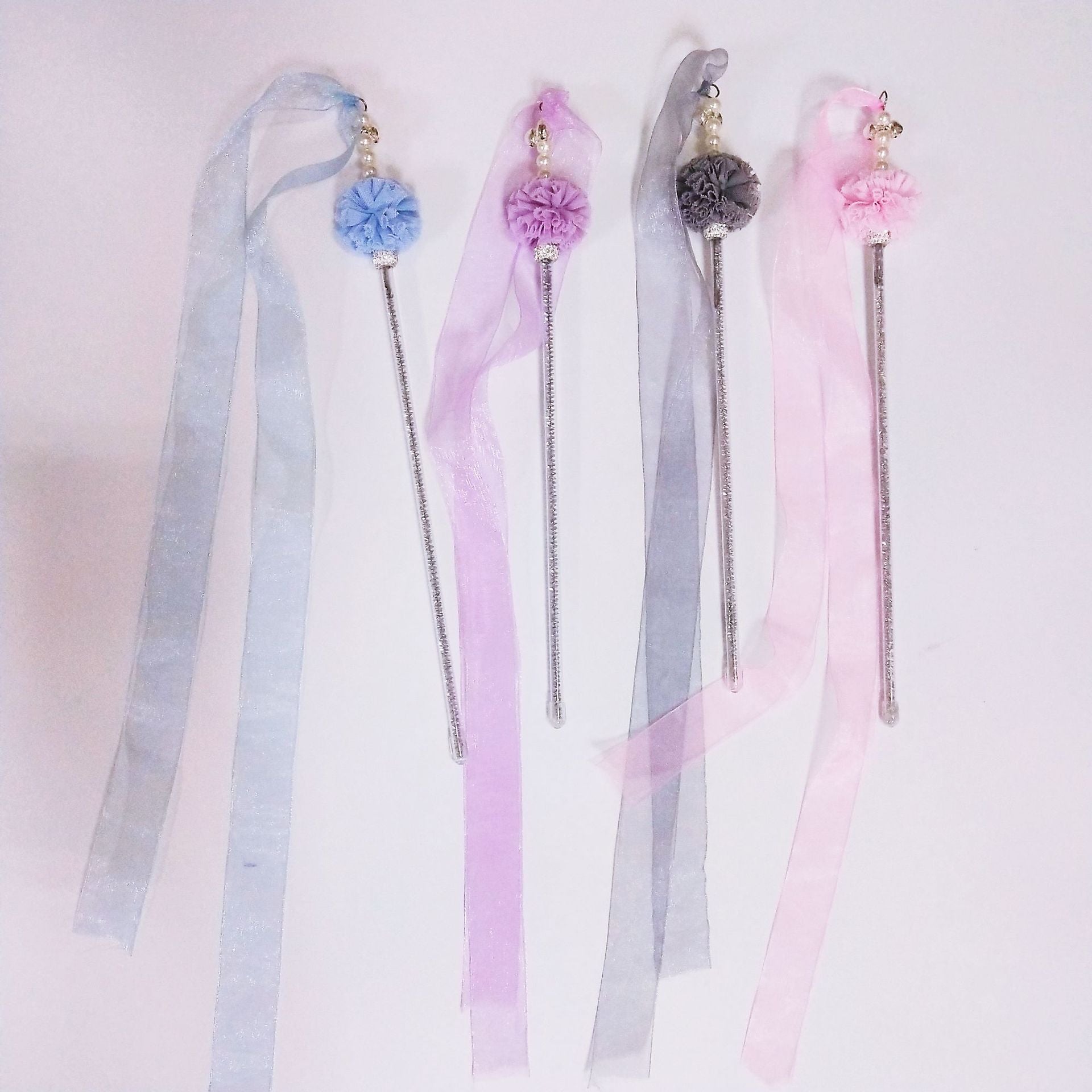 Four decorative hair sticks with ribbons on a light pink background