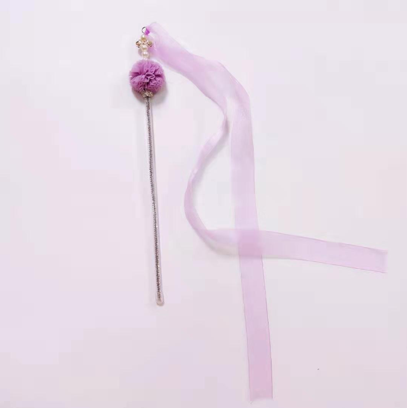 Decorative hair stick with a fluffy purple ball and a long pink ribbon on a light pink background