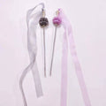 Two decorative hair sticks with ribbons on a light gray background