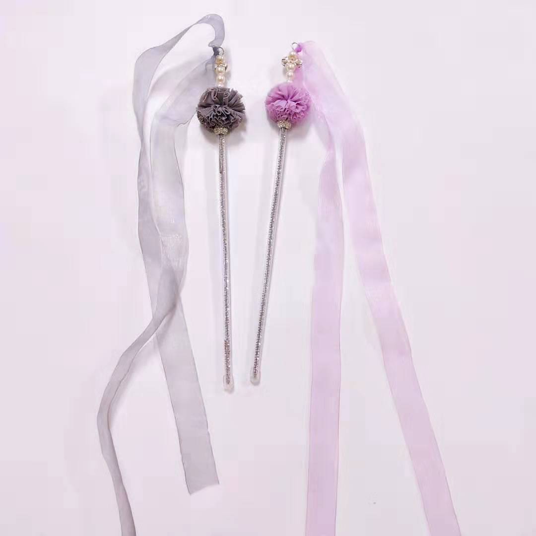 Two decorative hair sticks with ribbons on a light gray background